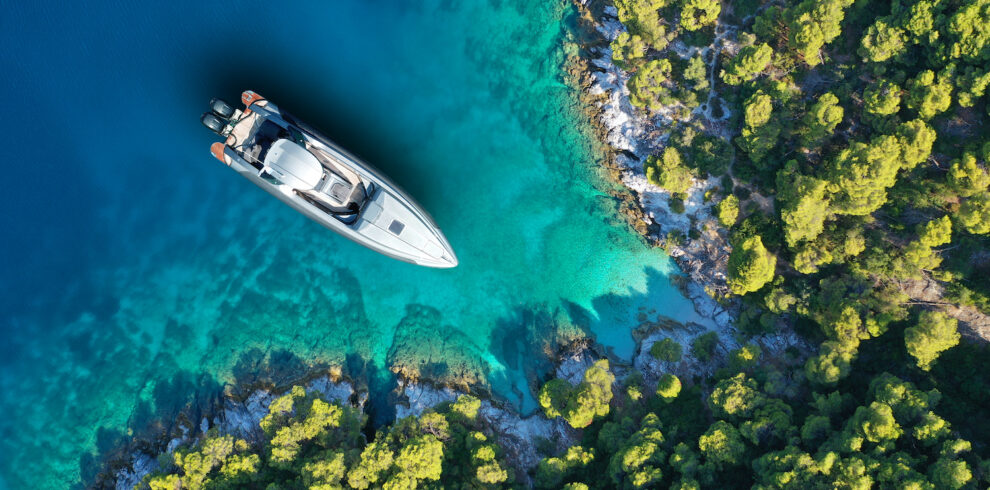 Aerial drone top down photo of inflatable speed boat anchored in tropical exotic island covered with pine trees